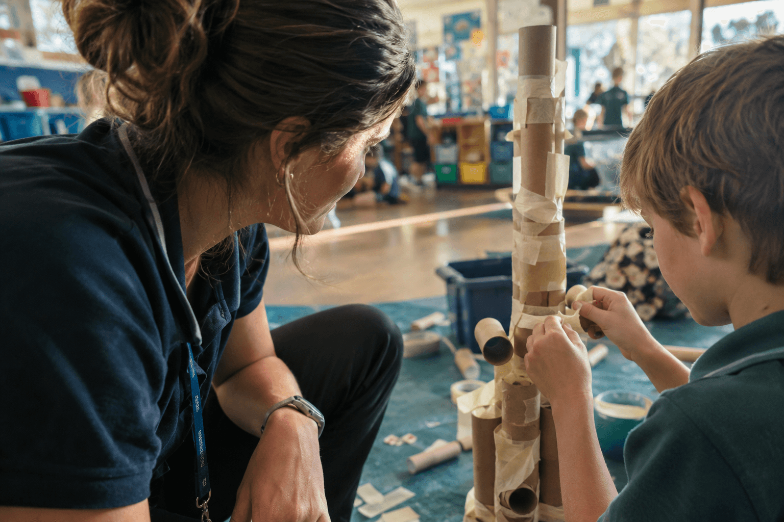 An educator watching a child build a tower from cardboard tubes and tape